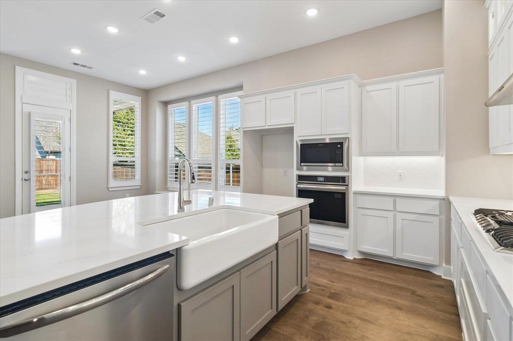 Kitchen featuring a large central island with a farmhouse-style apron sink, white quartz countertops, wood-finish flooring, recessed lighting, and built-in stainless steel double ovens