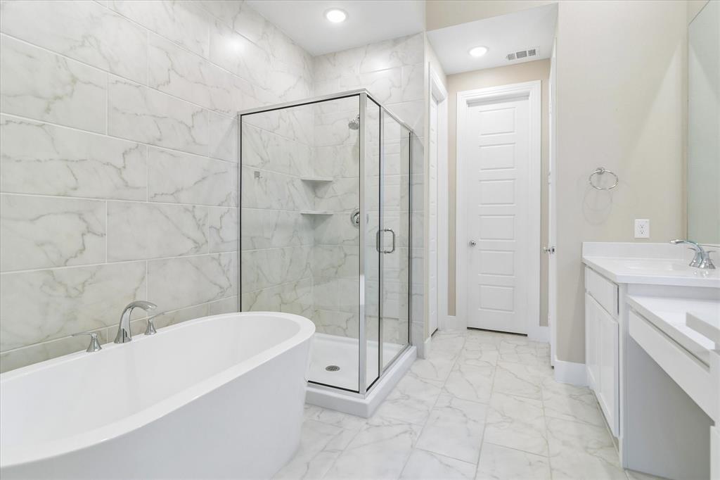 Freestanding white soaking tub, glass-enclosed shower with full-height stone-finish wall tile, white vanity cabinetry with surface-mounted sink, and stone-finish floor tiling