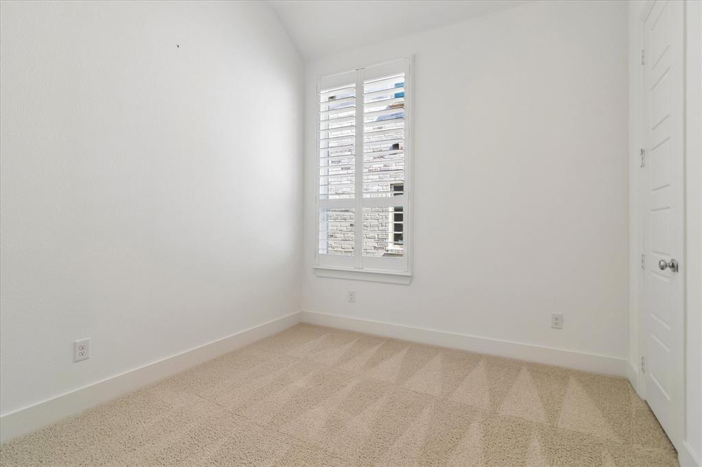 Neutral interior room featuring vaulted ceilings, light-toned carpeting, and a window with plantation-style shutters