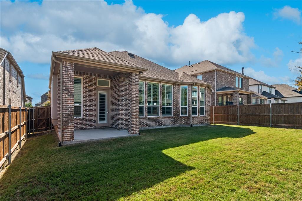Brick exterior, covered rear patio, multi-pane windows, and fenced backyard with a lawn