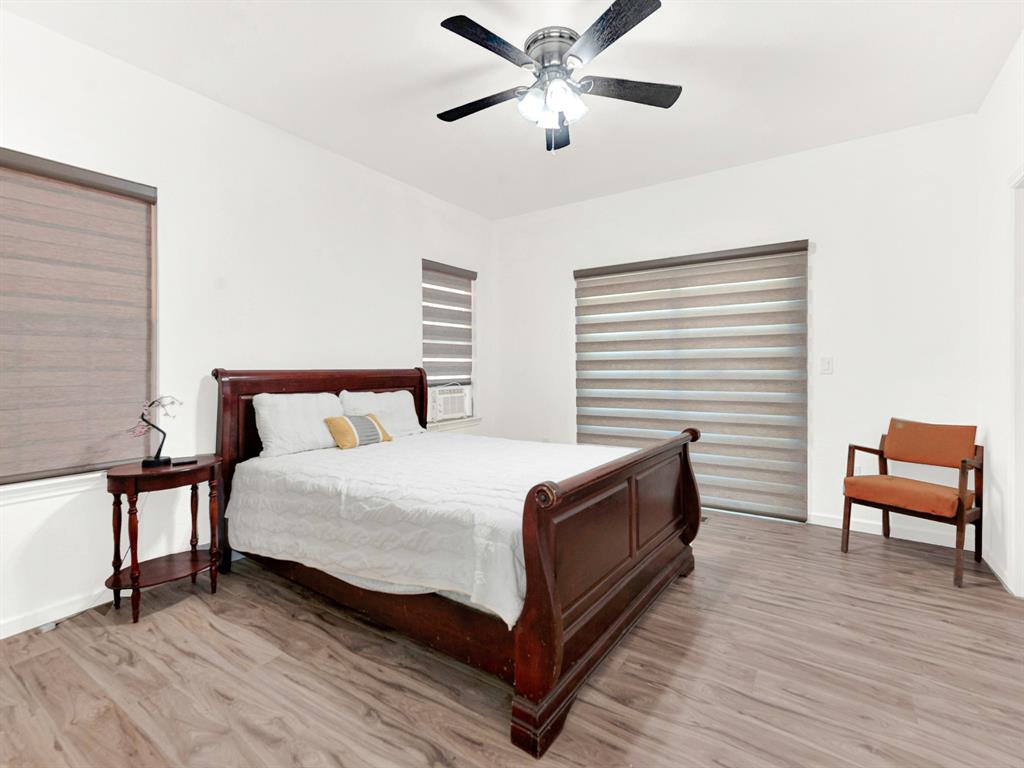 Neutral-toned wood-finish flooring, ceiling fan with integrated lighting, and multi-layered window shades