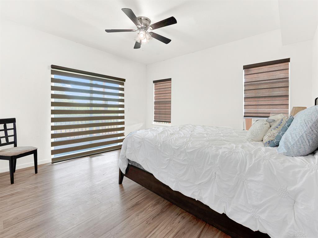 Neutral-toned walls paired with wood-finish flooring, accompanied by a multi-blade ceiling fan with integrated lighting and dual-tone window shades