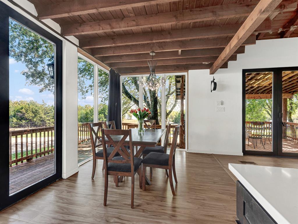 Exposed wood-beam ceiling, floor-to-ceiling windows, wood-finish flooring, and black-framed glass doors leading to an exterior deck