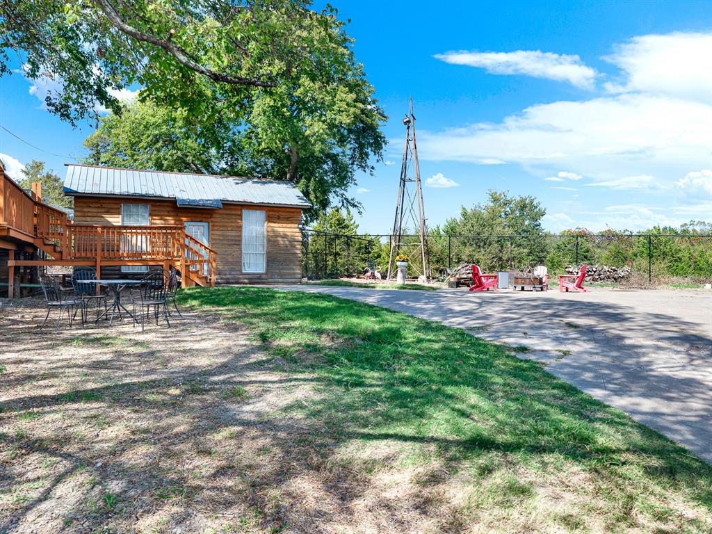 Exterior featuring a log-style cabin with a metal roof, an elevated wooden deck, a central metal windmill, and an expansive gravel grounds area