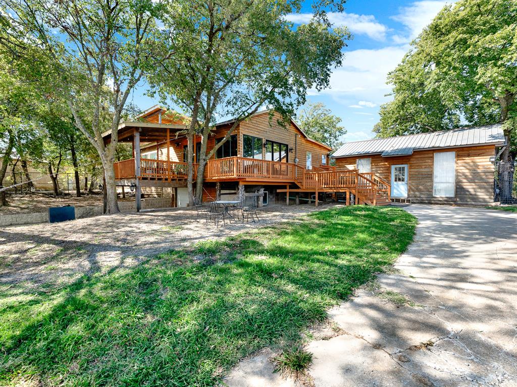 Exterior featuring wood siding, expansive wraparound elevated wood deck, metal roofing, concrete driveway, and mature tree canopy