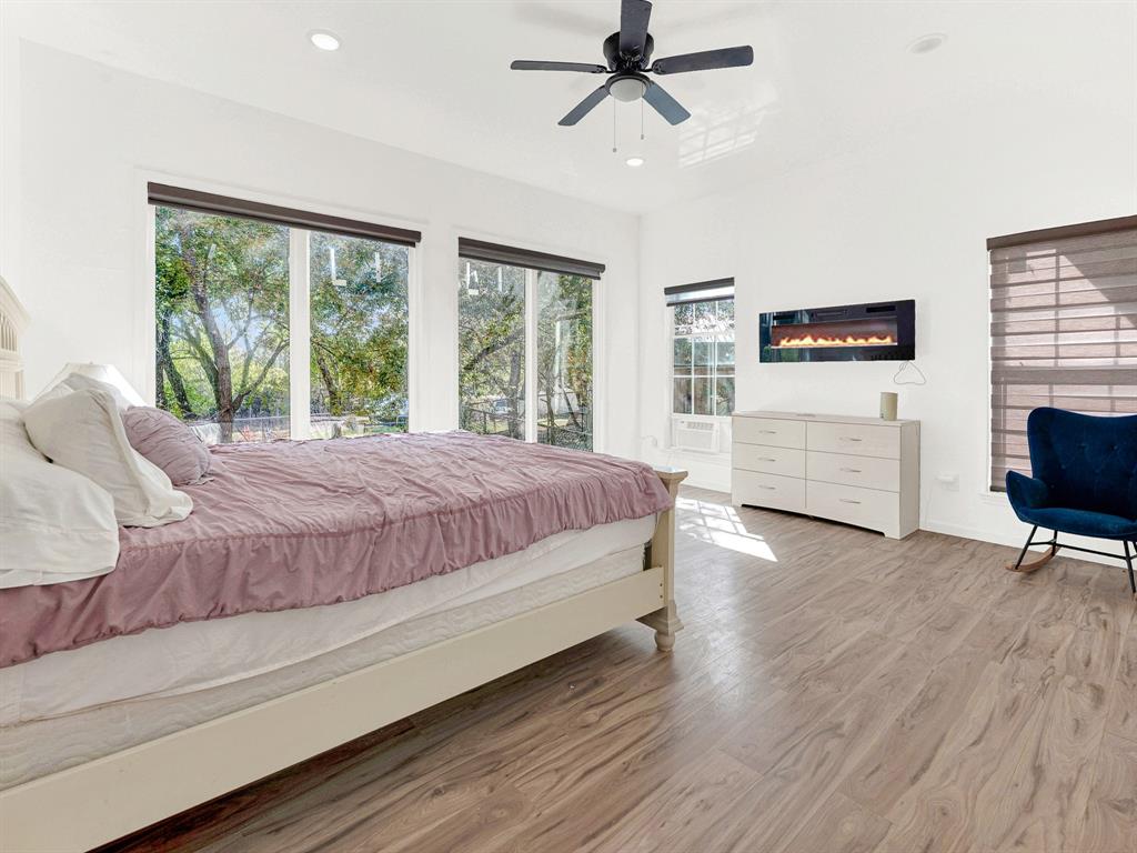 Wood-finish flooring, wall-mounted electric fireplace, ceiling fan, and large windows with integrated shades