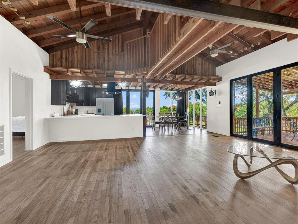 Vaulted ceiling with exposed wood beams, wood-finish flooring, floor-to-ceiling multi-panel glass doors, open-concept kitchen, and integrated ceiling fans