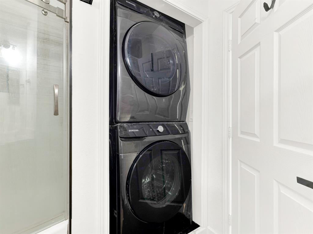 Stackable, front-load washer and dryer in a black finish, accompanied by a glass-panel shower door with a metallic pull handle and a white paneled door