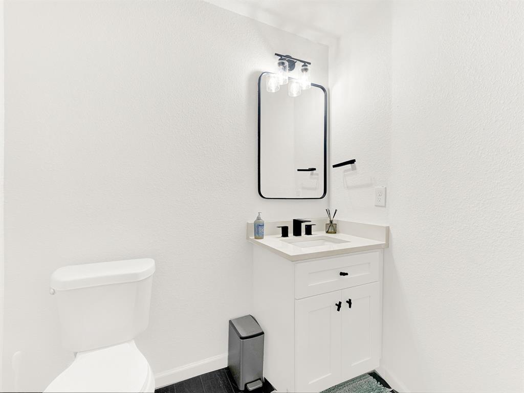 White vanity with stone-composite countertop, undermount sink, matte black widespread faucet, rectangular mirror with black frame, and matching three-light vanity fixture