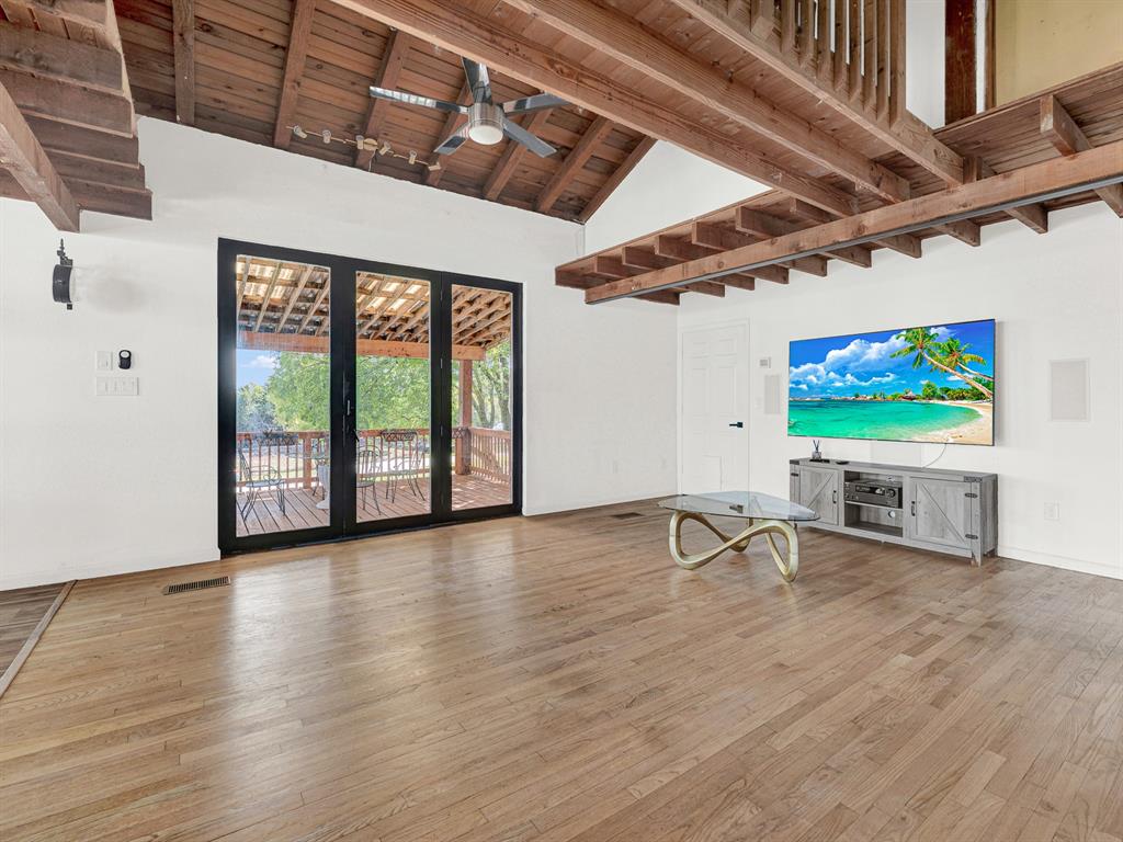 Vaulted ceiling featuring exposed wood beams, wood-finish flooring, multi-panel black-framed glass doors, and a ceiling fan