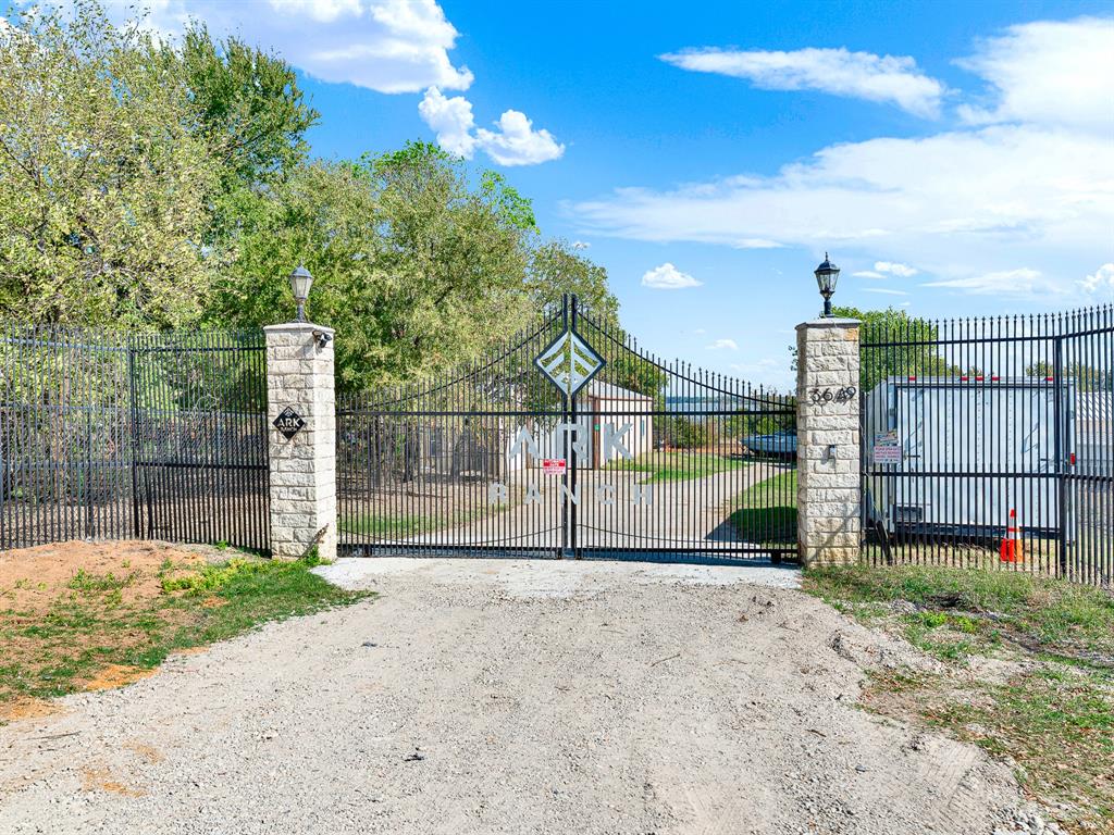 Gated entry featuring custom metal fencing, stone-clad pillars, and mounted post lighting