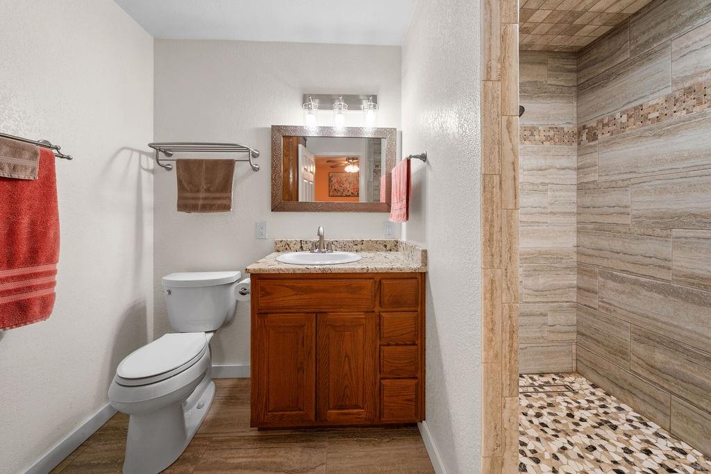 Bathroom featuring a wood-finish vanity with a stone countertop, an integrated sink, an expansive walk-in shower with decorative tile accents, and wood-finish flooring