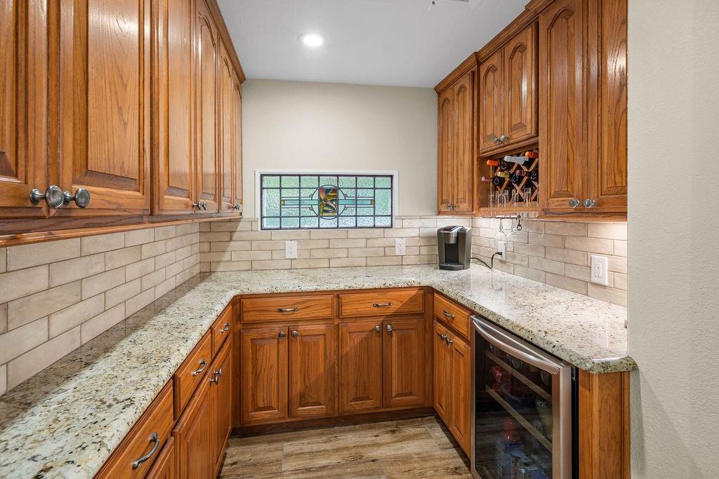 Custom cabinetry with integrated wine storage, stone countertops, subway tile backsplash, stained glass accent window, and built-in under-counter beverage refrigerator
