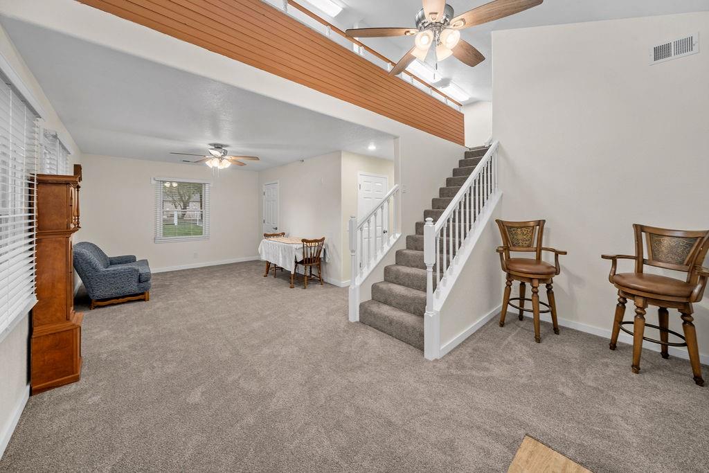 Vaulted ceilings, carpeted staircase with white balusters, wood-finish horizontal trim detail, dual ceiling fans, and neutral wall tones