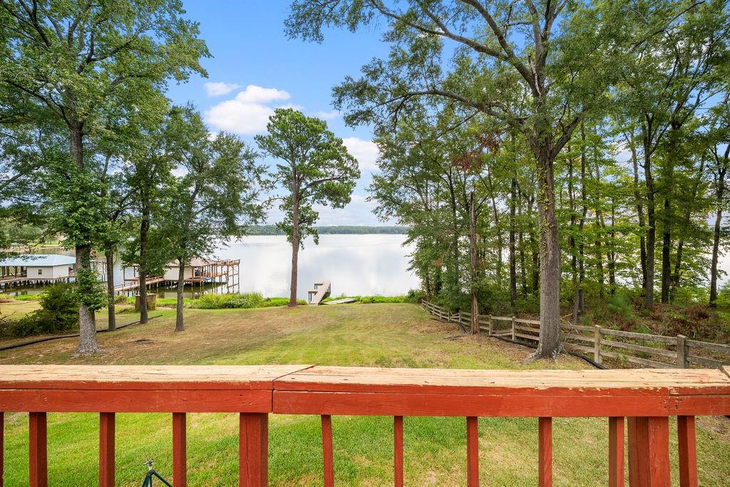 Elevated wood-railing deck overlooking a grassy backyard with mature trees, a wooden rail fence, and direct waterfront access including a private dock