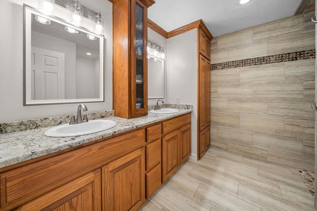 Double vanity featuring wood cabinetry, stone-patterned countertops, integrated storage tower, and dual undermount sinks with polished hardware