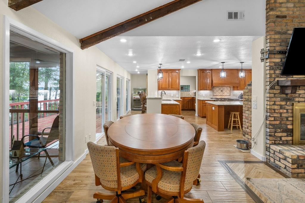 Vaulted ceilings with exposed wooden beams, brick-surround fireplace, wood-finish tile flooring, recessed lighting, and multiple sliding glass doors