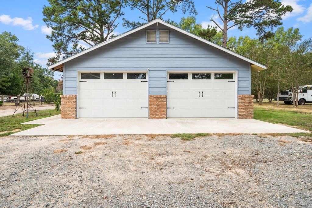 Detached two-car garage featuring blue horizontal siding, dual overhead doors with windows, brick pillar accents, and a concrete apron