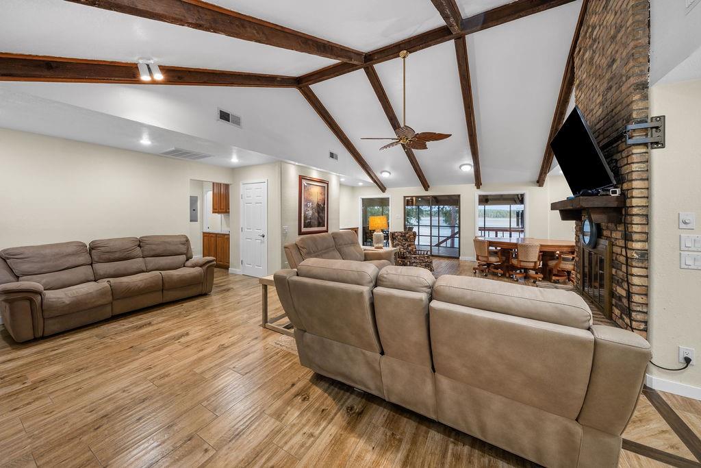 Vaulted ceiling featuring exposed wood-finish beams, wood-finish tile flooring, full-height brick fireplace with a wood mantel, and sliding glass doors