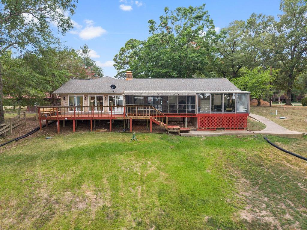 Exterior of the property featuring a raised wooden deck, a screened-in porch, brick siding, a concrete walkway, and expansive grounds