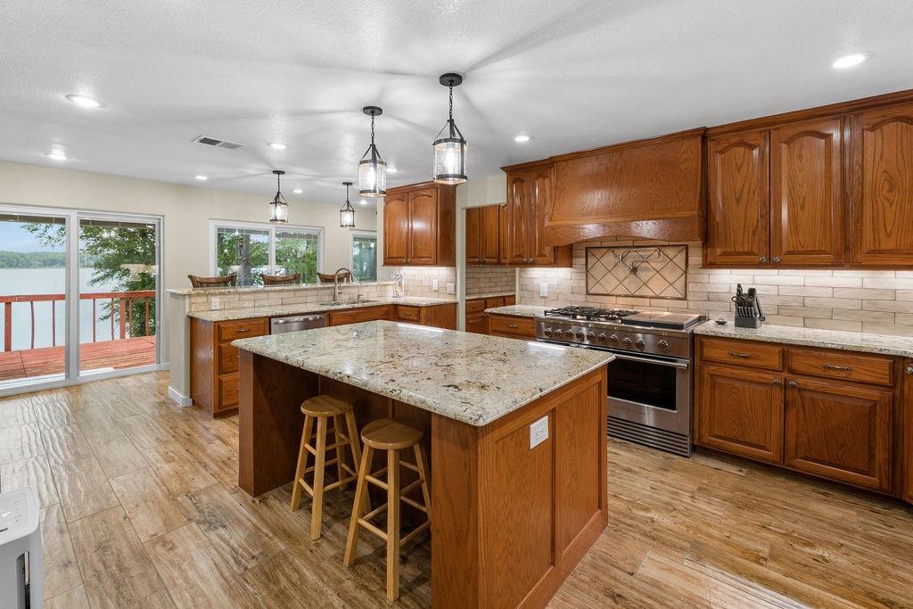 Kitchen featuring wood cabinetry, stone countertops, a center island, stainless steel range with a custom hood, and wood-finish flooring