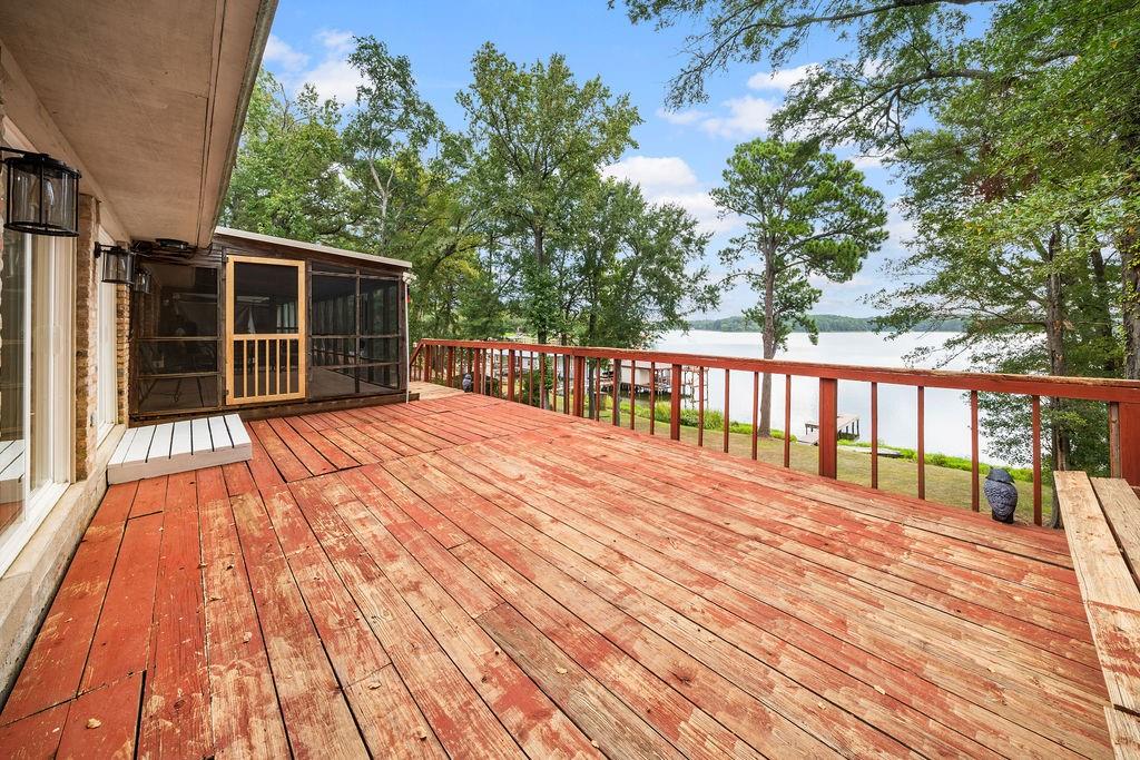 Expansive wood deck featuring a screened-in porch, built-in wooden bench, and water frontage