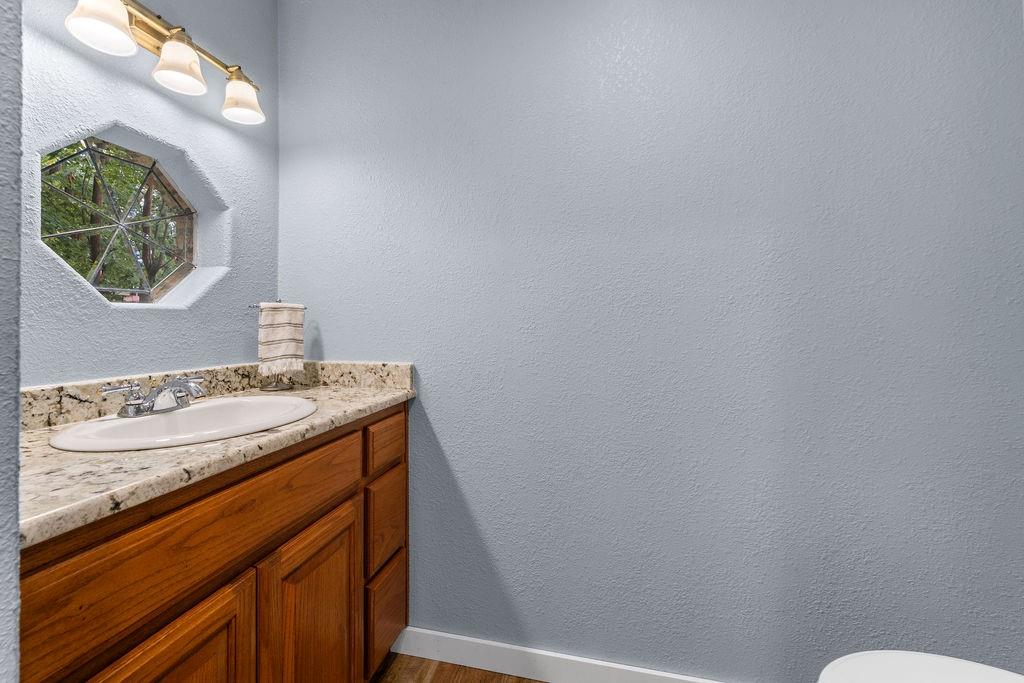 Natural stone-surface vanity with an integrated oval sink, wood-finish cabinetry, hexagonal accent window, and three-bulb vanity lighting fixture