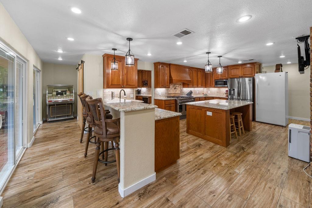 Kitchen featuring custom wood cabinetry, stone countertops, central island, wood-finish flooring, and pendant lighting