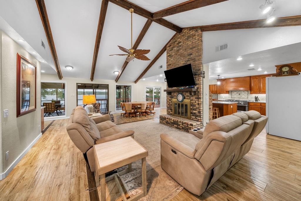 Vaulted ceiling with exposed wood beams, brick fireplace featuring a wooden mantel, and wood-finish flooring