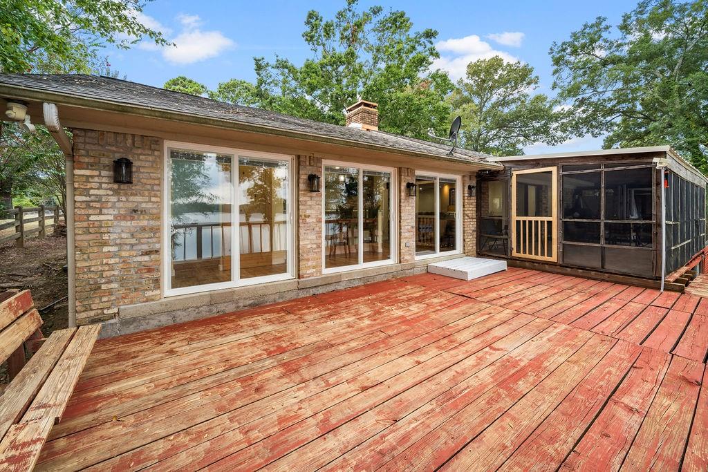 Exterior featuring brick facade, expansive wood deck, attached screened-in porch, and sliding glass door entries