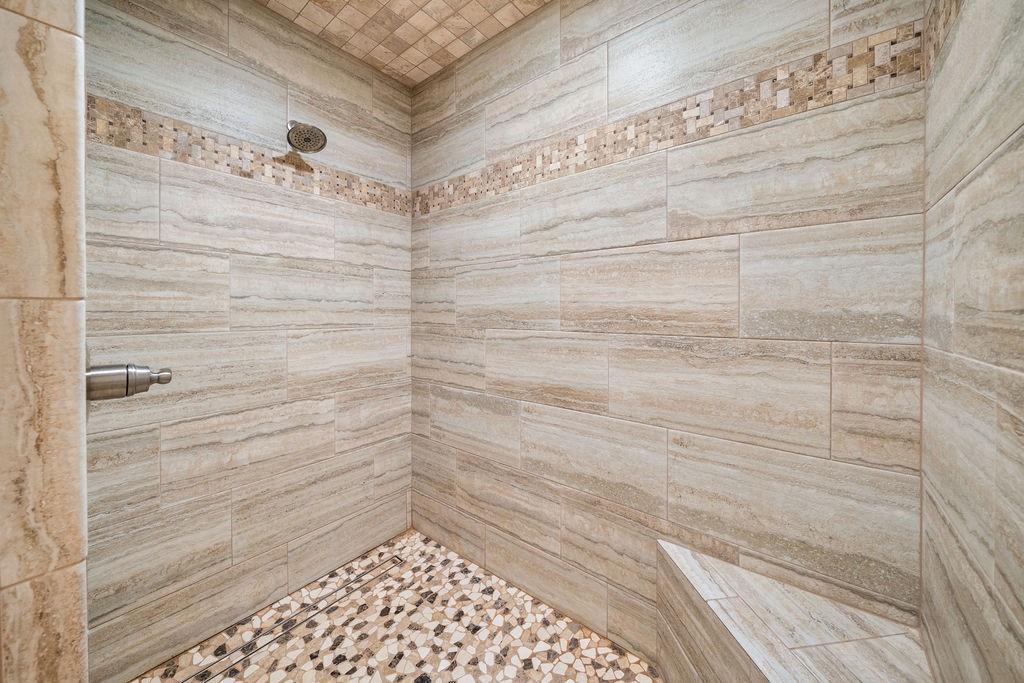 Walk-in shower featuring floor-to-ceiling stone-finish wall tile, a decorative mosaic tile inlay, a built-in corner bench, a pebble-finish floor, and a metal shower head