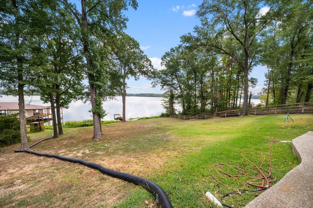 Waterfront lot featuring a grass lawn, mature trees, and wooden perimeter fencing