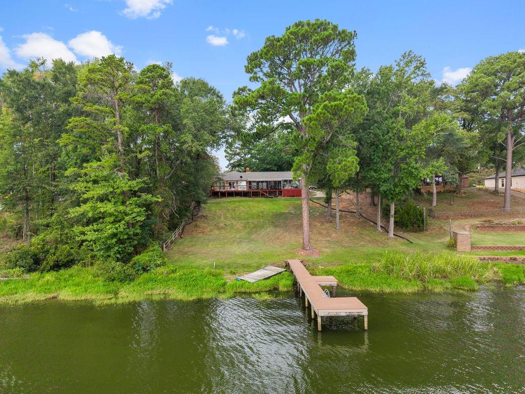 Waterfront property featuring a private wooden pier, expansive sloped lawn, mature trees, and a raised exterior deck