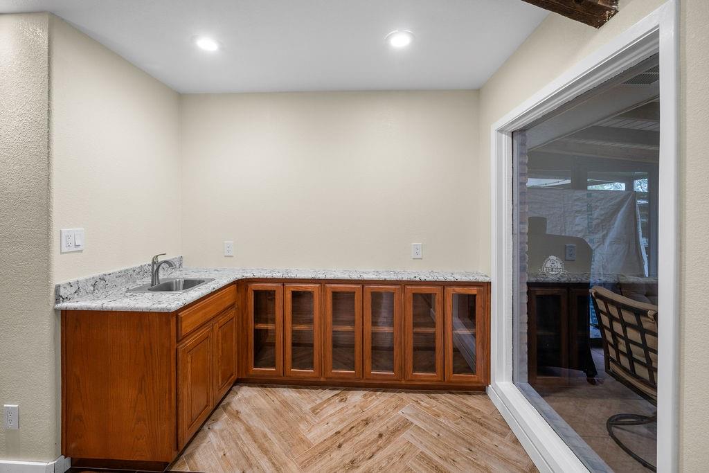 Custom cabinetry featuring glass-panel doors, light-toned stone countertop, stainless steel undermount sink with arched faucet, and wood-finish flooring in a herringbone pattern