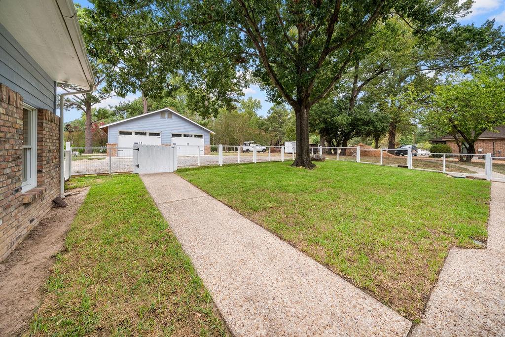 Fenced backyard featuring a concrete walkway, mature trees, a detached two-car garage, and brick and siding exterior cladding