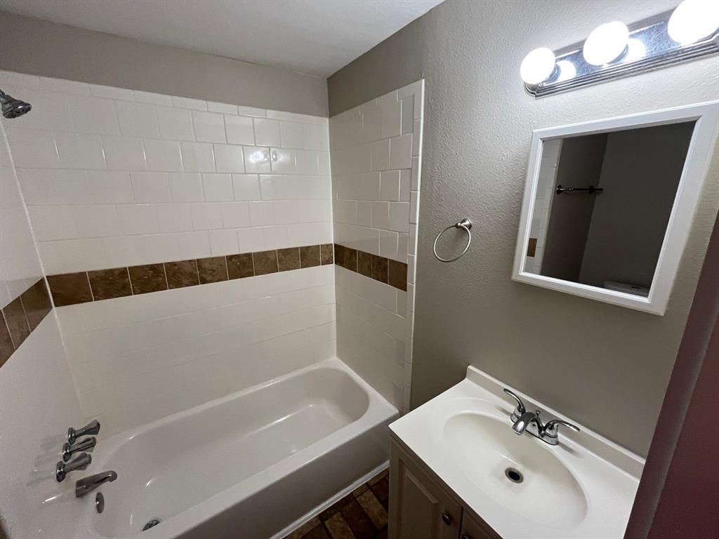 Bathroom featuring a tub-shower combination with decorative tile inlay, vanity with integrated basin, multi-bulb wall-mounted lighting, and a framed mirror