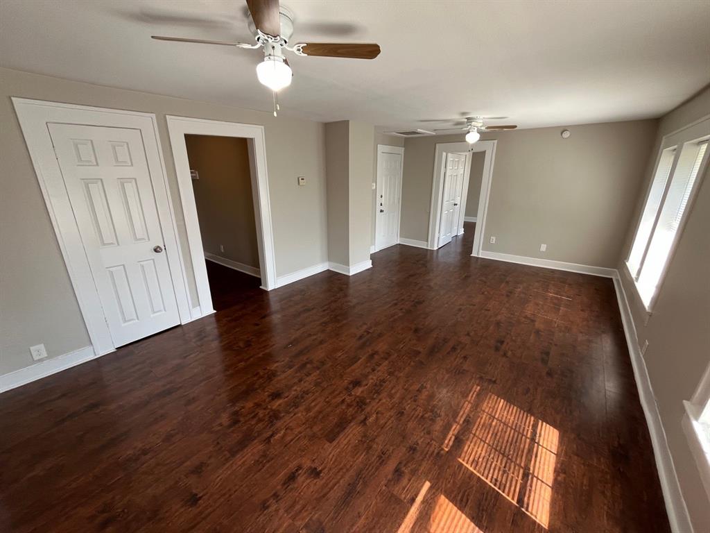 Spacious room featuring dark wood-finish flooring, two ceiling fans with integrated lighting, neutral wall paint, and white paneled doors