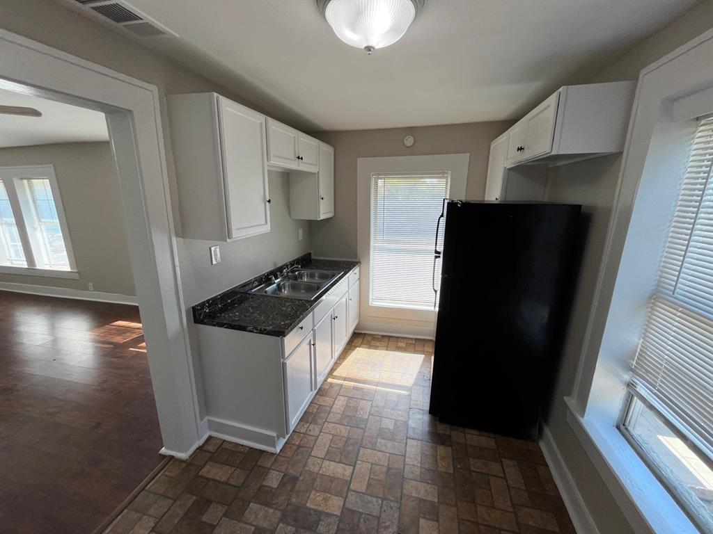 Kitchen featuring white cabinetry, dark stone-patterned countertops, a double-basin stainless steel sink, and mosaic-tiled flooring