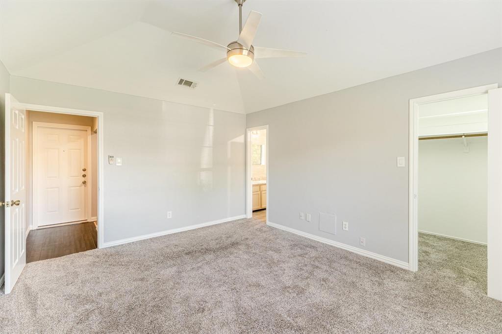 Vaulted ceiling featuring a central brushed-nickel ceiling fan with integrated lighting, wall-to-wall carpeting, and a walk-in closet with built-in shelving