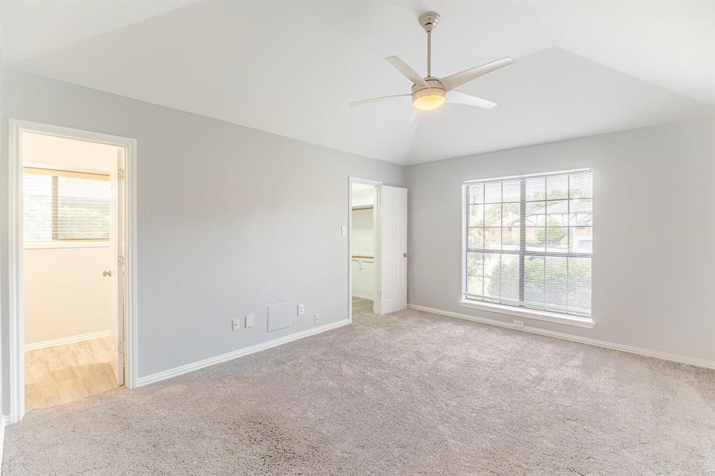 Vaulted ceiling with a central brushed-nickel ceiling fan, neutral wall-to-wall carpeting, and a multi-pane grid window