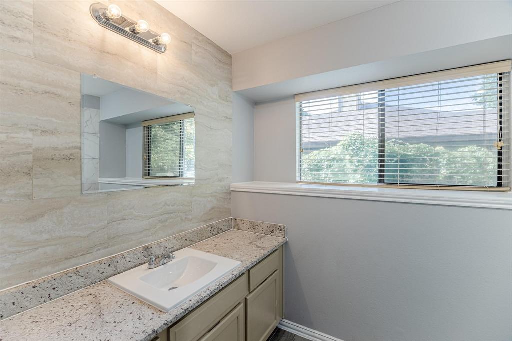 Vanity featuring a stone-look countertop, integrated sink, neutral-toned cabinetry, floor-to-ceiling textured wall tile, and a three-bulb light fixture