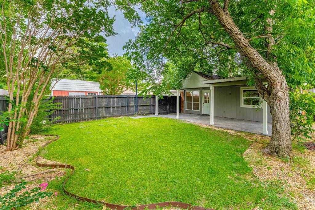 Backyard featuring a covered patio, mature shade trees, perimeter wood fencing, and a manicured lawn