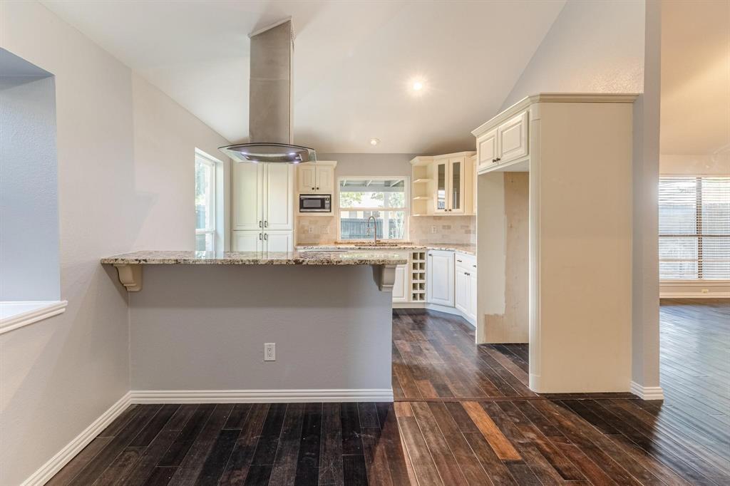 Kitchen featuring stone countertops, white cabinetry, a built-in wine rack, stainless steel chimney-style range hood, and dark wood-finish flooring