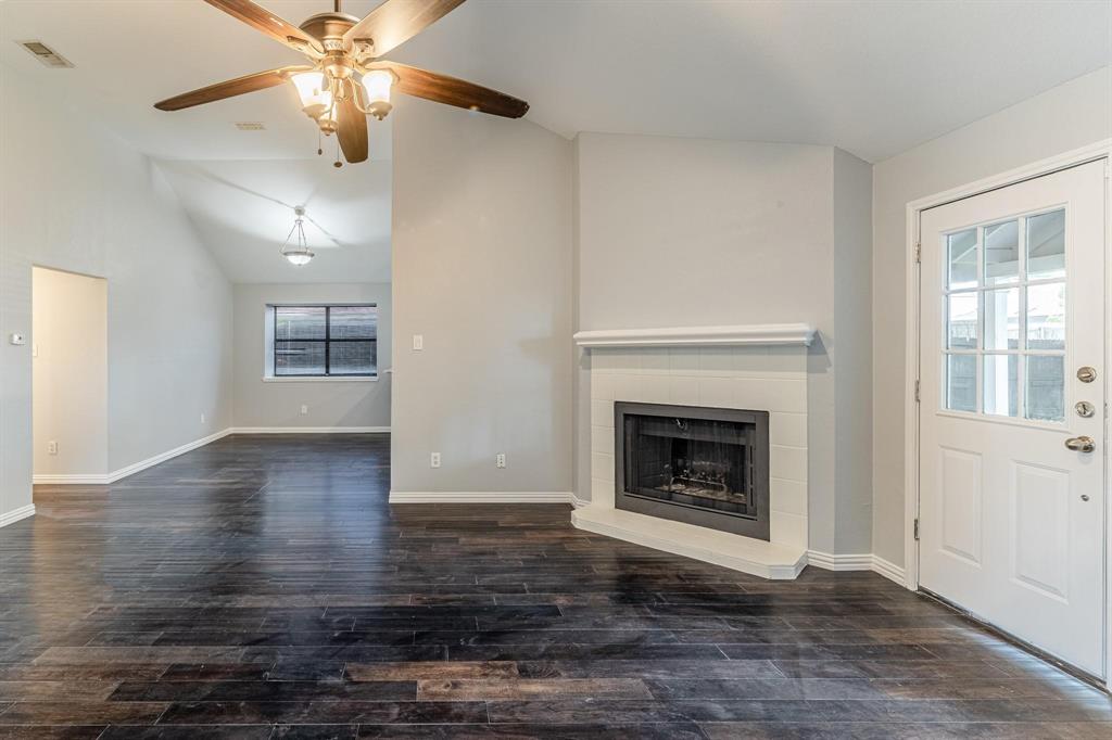 Vaulted ceilings, wood-finish flooring, corner fireplace with white tile surround, ceiling fan, and multi-lite glass panel door