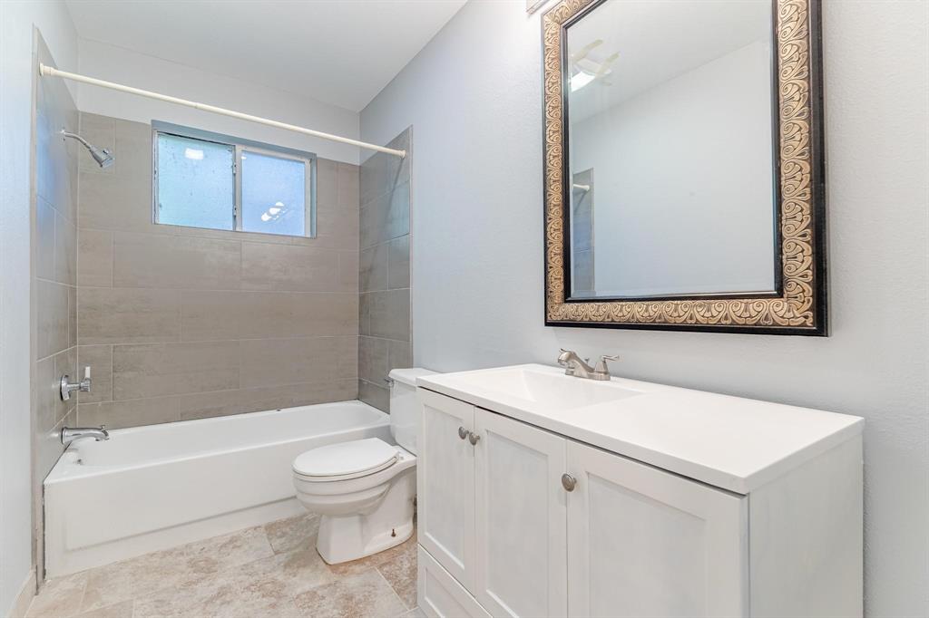 Bathroom featuring a white vanity cabinet with a solid surface countertop, rectangular under-mount sink, tile tub surround, and tile flooring