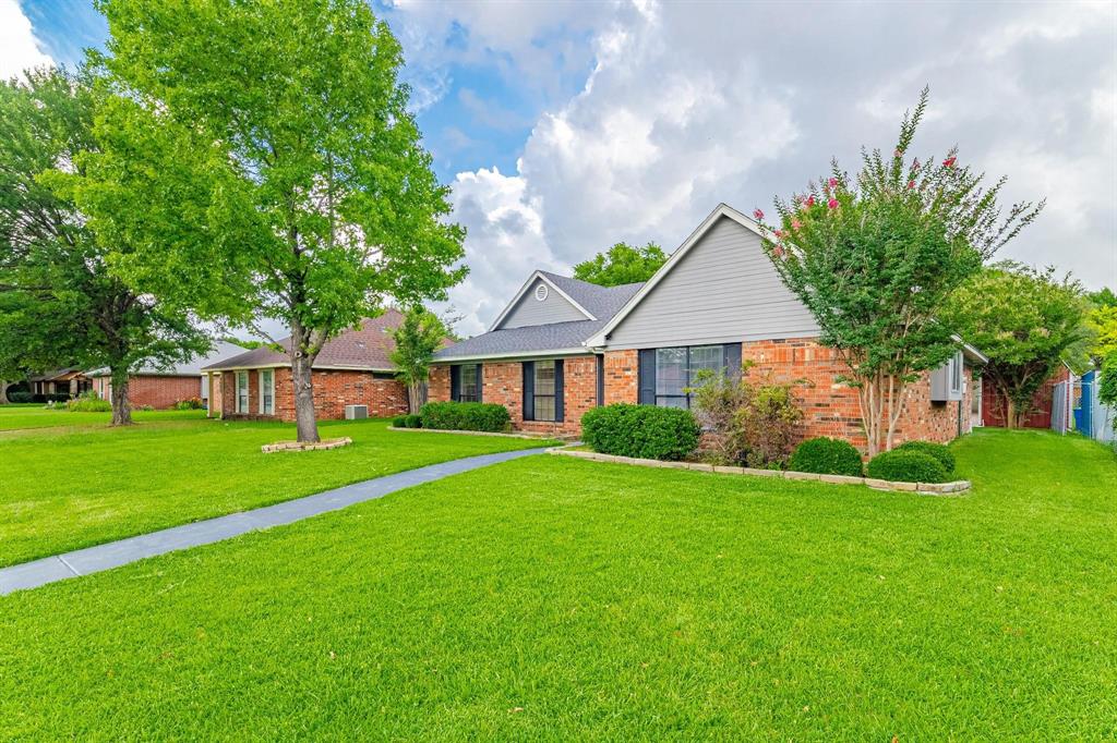 Single-story residence featuring a brick and horizontal siding exterior, dual-gable roofline, concrete walkway, and manicured landscaping with mature trees
