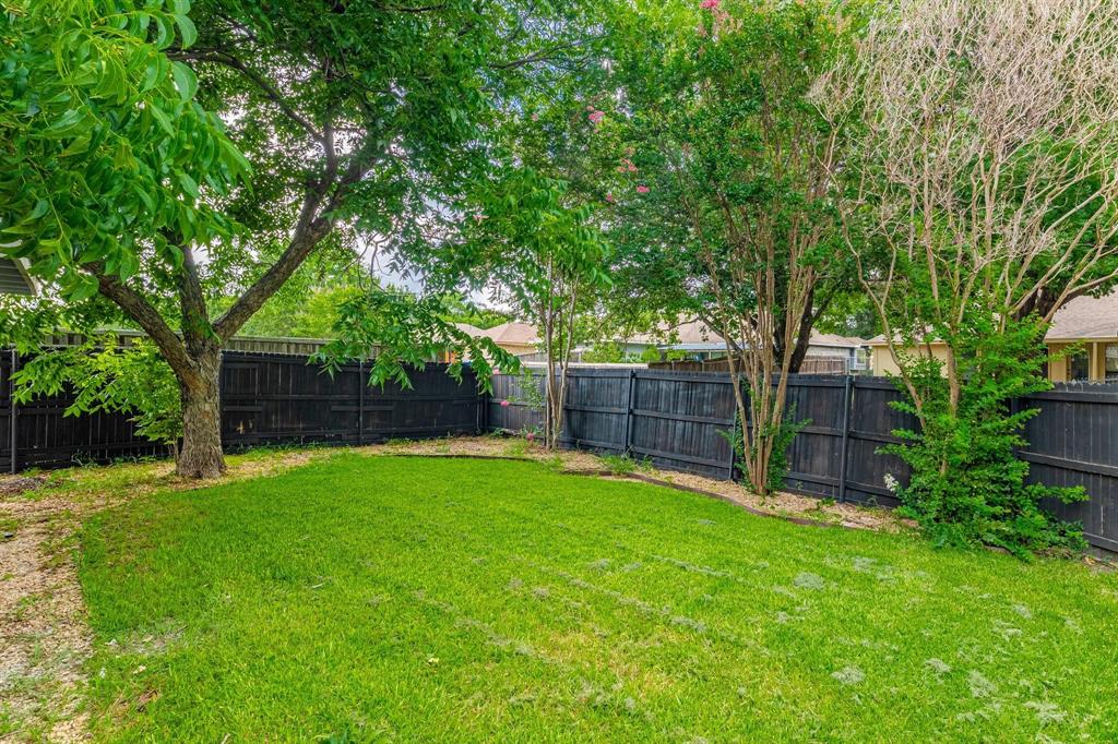 Fenced backyard featuring established shade trees, a grass lawn, and mature ornamental plantings