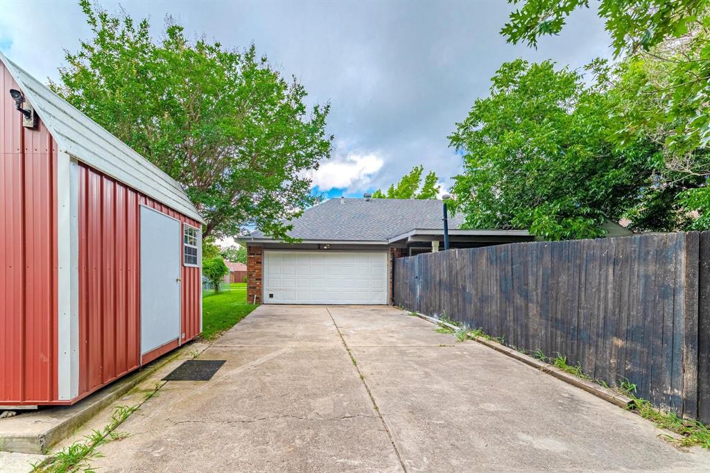 Concrete driveway with an attached garage, featuring a metal storage structure and privacy fencing