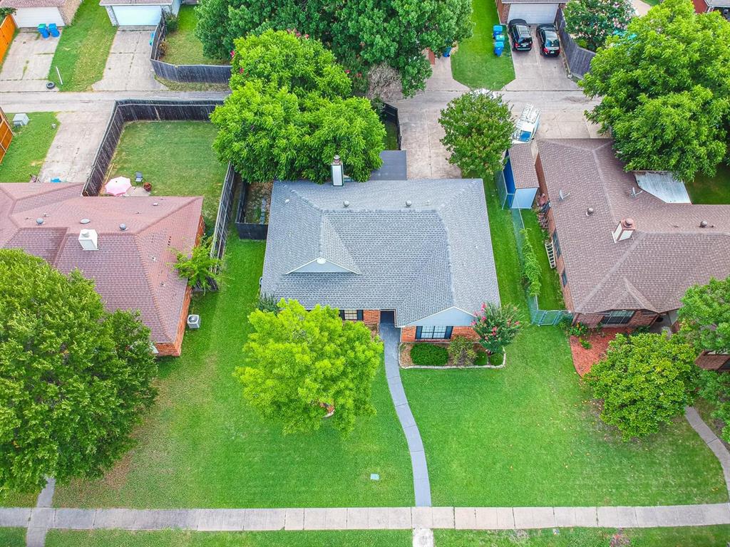 Aerial perspective featuring a brick exterior, gabled roof, concrete walkway, and mature trees on a level lot