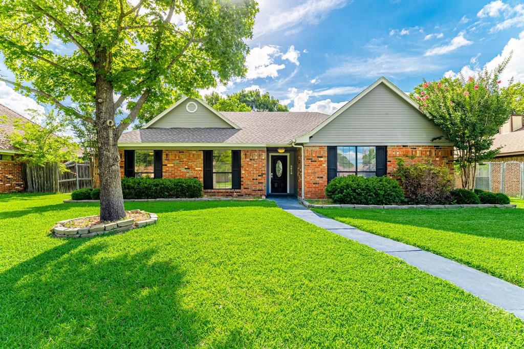 Single-story residence with a brick and horizontal siding facade, featuring a gabled roofline, concrete walkway, and mature landscaping
